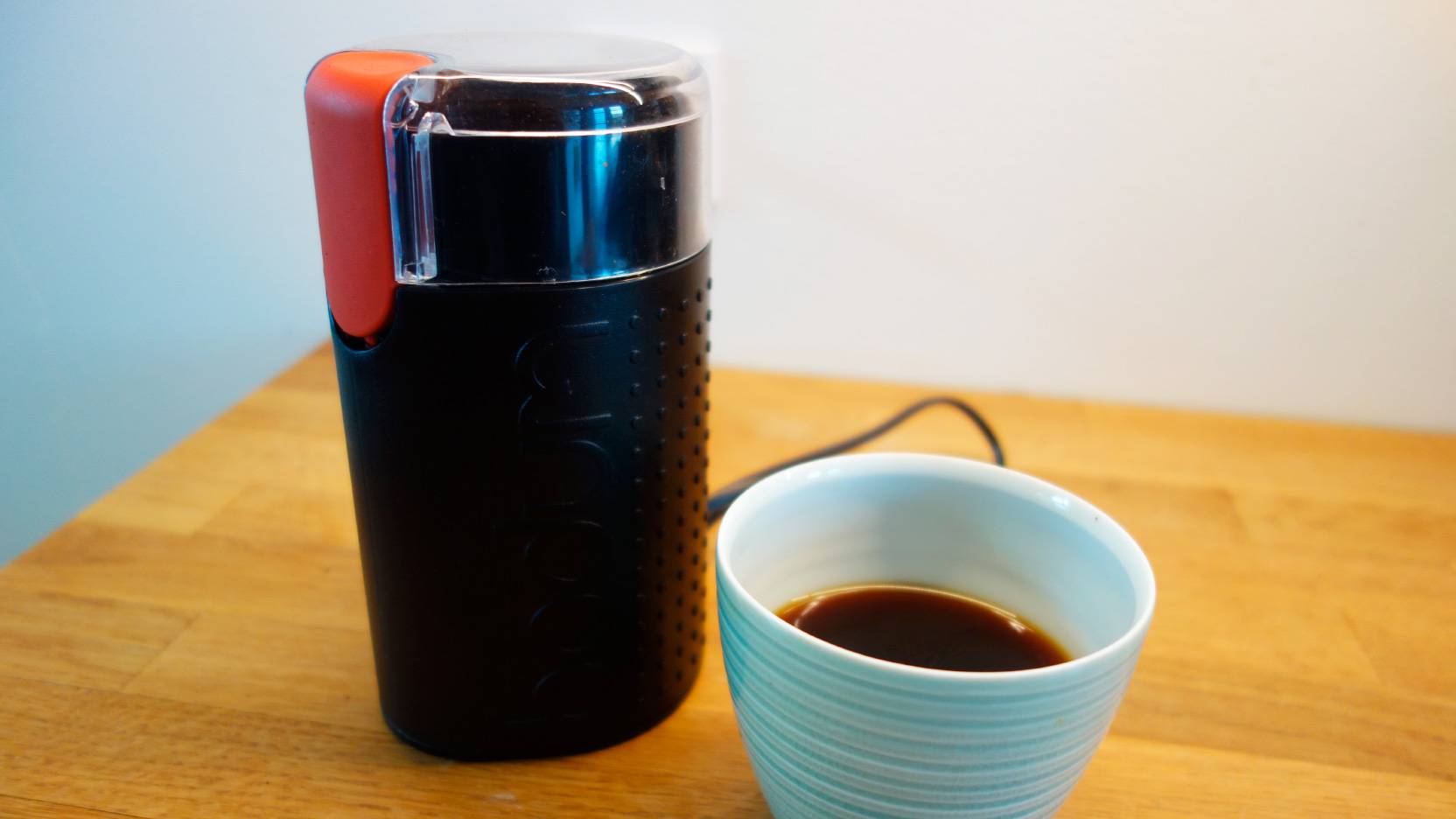 Image of the black Bodum Bistro coffee mill next to a freshly brewed cup of coffee