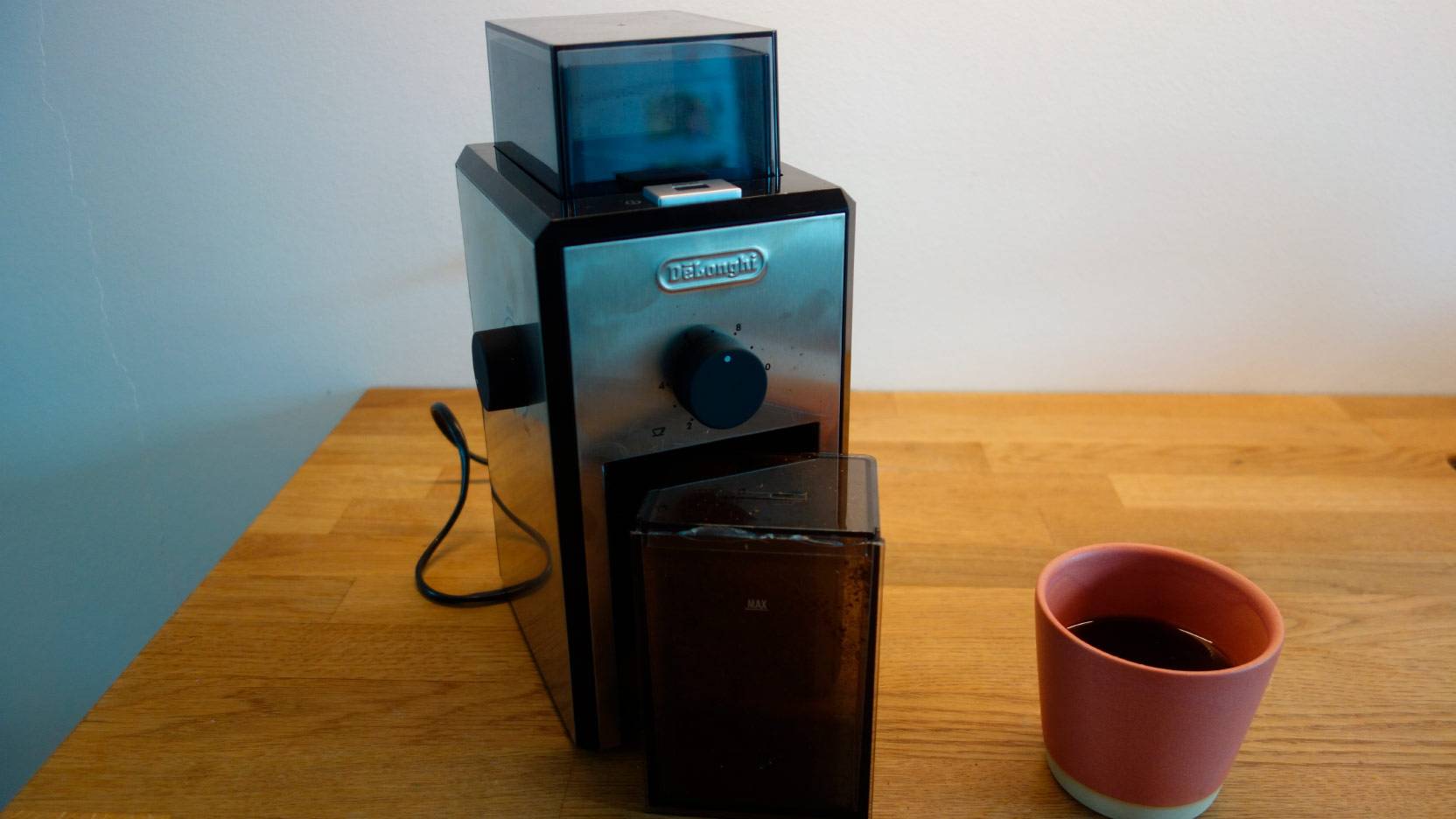 Image of Delonghi KG89 coffee grinder on the worktop with a pink cup of coffee
